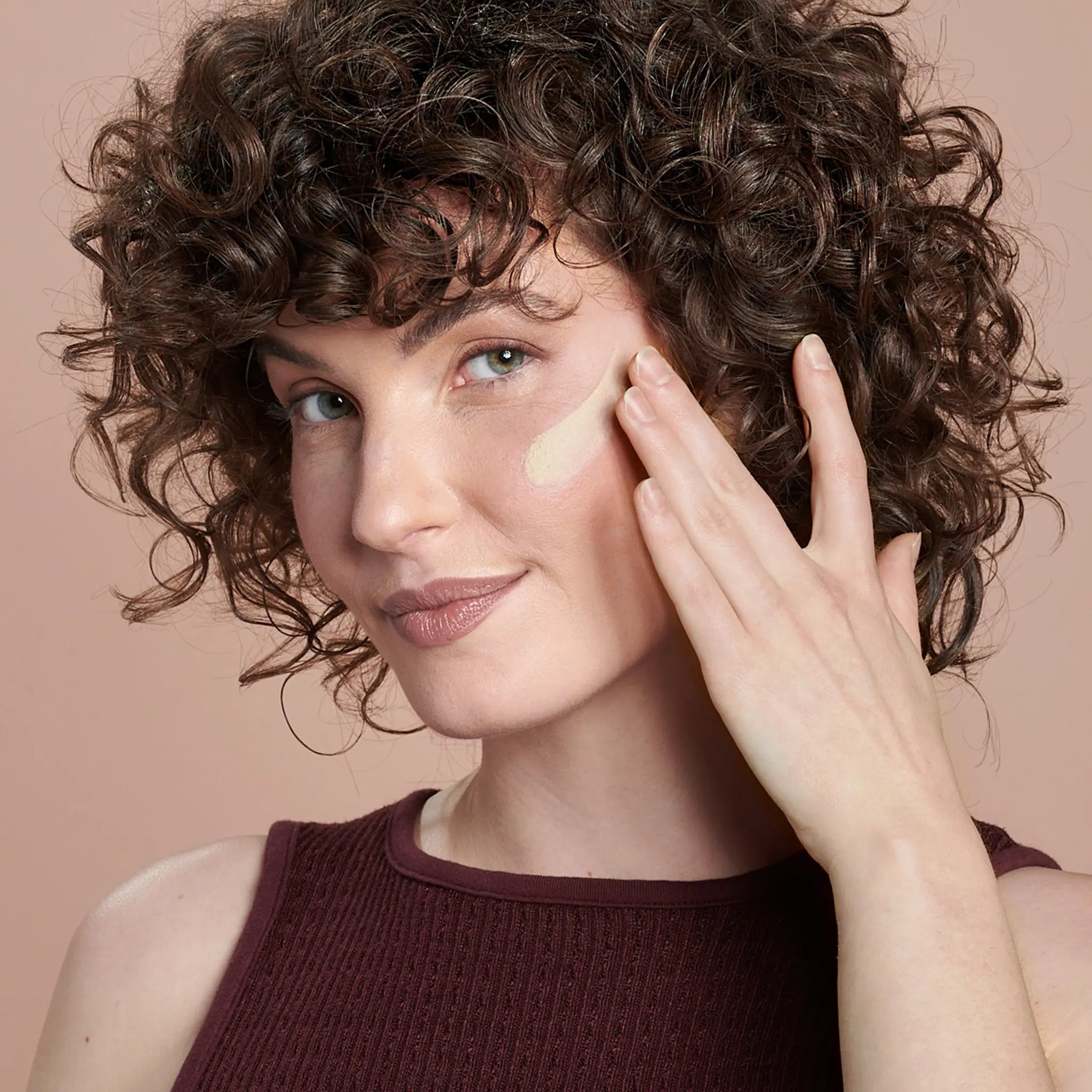 Female model with swatch of All Calm® Clinical Redness Corrector SPF 50 on cheek || all